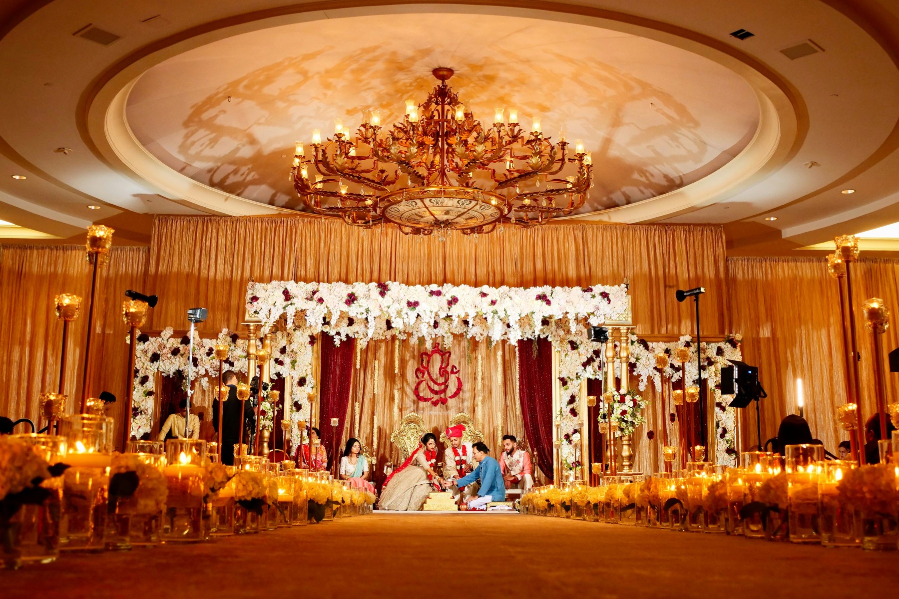 Grand ballroom wedding mandap with gold chandelier and floral arch by SGR Decorators